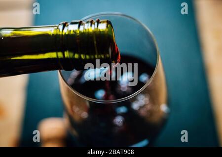 Nahaufnahme von Rotwein, der aus einer Flasche in ein Weinglas gegossen wird. Ansicht von oben. Verschwommener Hintergrund, geringe Schärfentiefe Stockfoto
