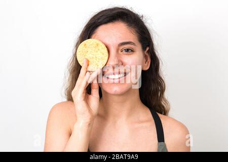 Junge fröhliche Frau mit geschweiften Haaren, die natürlich aussieht und ihr Gesicht mit Schwamm wäscht Stockfoto