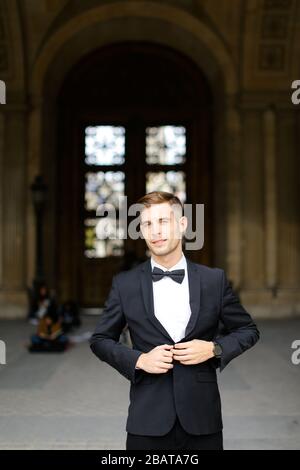 Junger europäischer Mann steht und posiert, trägt schwarzen Anzug und Krawatte. Stockfoto