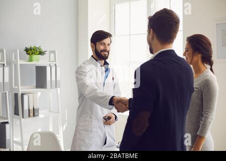 Selbstbewusster Arzt und paarter Patient sitzen am Tisch in der Klinik. Hausarzt. Stockfoto