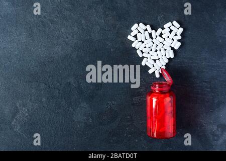 Pillen in Herzform und rote Pillenflasche Draufsicht auf schwarzem Hintergrund. Pillen zur Behandlung der Herzerkrankung. Kopierbereich. Stockfoto