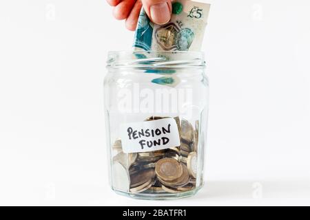 Ein Glaskerl mit britischen Münzen, mit einem handschriftlichen Etikett "Pensionsfonds", eine männliche Hand mit einer Note von £5 Stockfoto