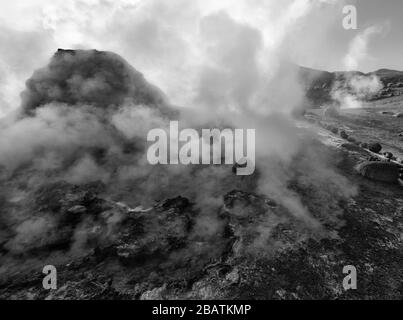 Dampf steigt aus einem Geysir um einen Felsbrocken bei Sonnenaufgang, El Tatio Geyser Field, Atacama-Wüste, Chile (Schwarzweiß) Stockfoto