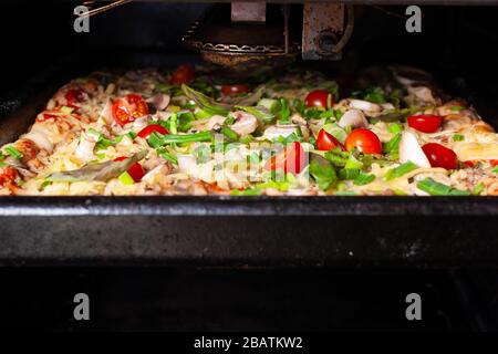 Frische rohe Pizza mit Pilzen, Kirschtomaten, Basil und Parmesan in einer rechteckigen Pfanne im Ofen. Hausgemachte Pizza vor dem Backen Stockfoto