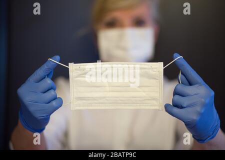 Seniorin trägt Maske, Handschuhe hält eine Maske in den Händen. Selektiver Fokus. Coronavirus und epidemische Virussymptome. Stockfoto