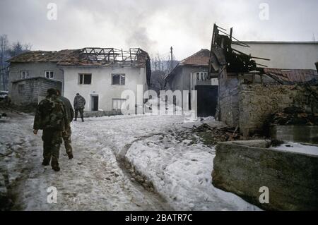 Januar 1994 während des Krieges in Zentralbosnien: Noch immer zerschlägende Häuser, während Soldaten der Rama Brigade der HVO durch das bosnisch-muslimische Dorf hier spazieren, das zwei Tage zuvor gefangen genommen wurde. Stockfoto