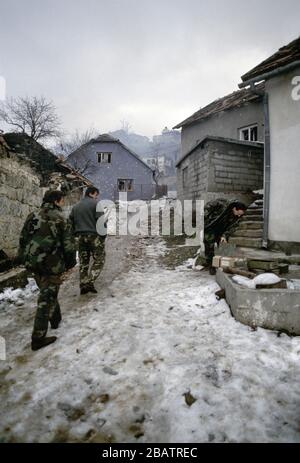 Januar 1994 während des Krieges in Zentralbosnien: Noch immer zerschlägende Häuser, während Soldaten der Rama Brigade der HVO durch das bosnisch-muslimische Dorf hier spazieren, das zwei Tage zuvor gefangen genommen wurde. Stockfoto