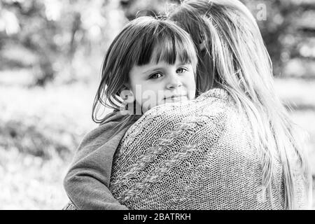 Schwarz-weißer Schuss von junger schöner Frau beruhigt sich und umarmt ihre traurige Tochter, während sie draußen steht. Kleines enttäuschtes Mädchen, das ihn umarmte Stockfoto