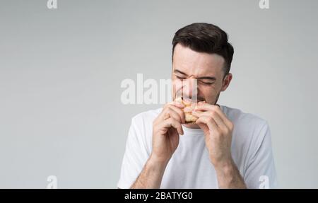 Junger Mann isoliert über Hintergrund. Bild von Kerl, der Burger isst und beißt. Leckere köstliche fettige Mahlzeit. Essen mit Vergnügen. Keine Schuld dafür Stockfoto