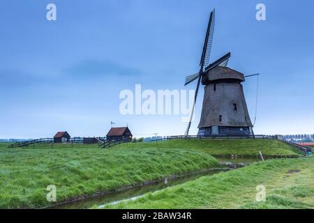 Grüne Rasenfelder und eine Windmühle spiegelten sich in der Abenddämmerung im Kanal wider. Berkmeer, Koggenland, Nordholland, Niederlande, Europa. Stockfoto