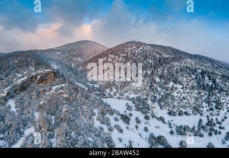 Der Luftblick über einen Sonnenuntergang über dem Berg in Arahova, Griechenland, ein Blick auf das Tal unten mit von Schnee bedeckten Bäumen, Farben des Sonnenuntergangs Stockfoto