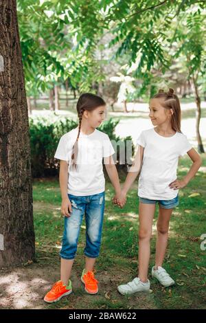 Zwei kleine Mädchen in weißen T-Shirts stehen im Park im Freien. Verspotten Sie sich. Stockfoto