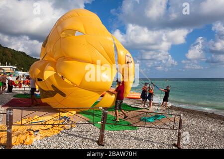 SOTSCHI, RUSSLAND-CIRCA Jun, 2018: Menschen machen sich bereit, mit einem per Boot gezogenen Seil zu parasieren. Laufen und starten vom Strand. Gelber Fallschirm Stockfoto