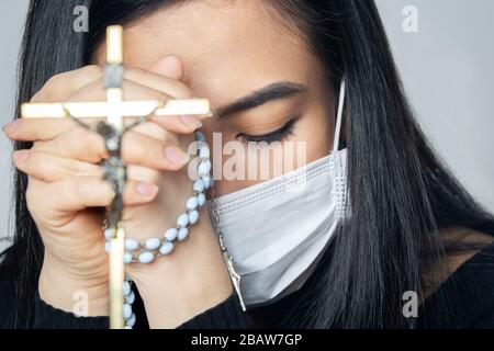 Eine Frau mit medizinischer Maske, die über die globale Coronavirus-Pandemie betet, um Angst und Depression zu reduzieren. Frau mit Rosenkranz. Stockfoto