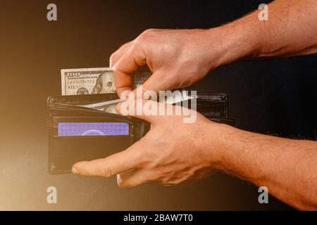 Der Mann auf schwarzem Hintergrund hält eine Geldbörse mit Dollar-Nahaufnahme in seinen Händen. Stockfoto