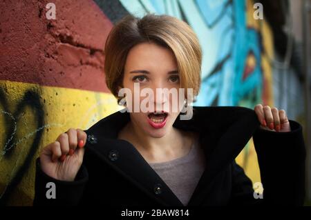 Weibliches Porträt des jungen Mädchens mit kurzen blonden Haaren in der Nähe der Wand mit Graffiti. Jugendkultur, Street-Art-Konzept Stockfoto