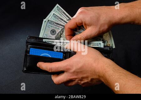 Der Mann auf schwarzem Hintergrund hält eine Geldbörse mit Dollar-Nahaufnahme in seinen Händen. Stockfoto