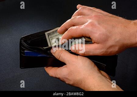 Mann entfernt Dollar von seiner Brieftasche, seinen Händen und seiner Brieftasche auf schwarzem Hintergrund. Stockfoto