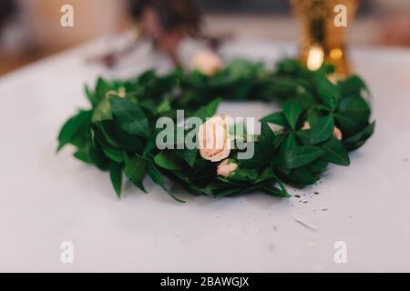 Kranz mit grünen Blättern und rosa Rosen auf weißem Grund. Hochzeitskrone. Selektiver Fokus Stockfoto