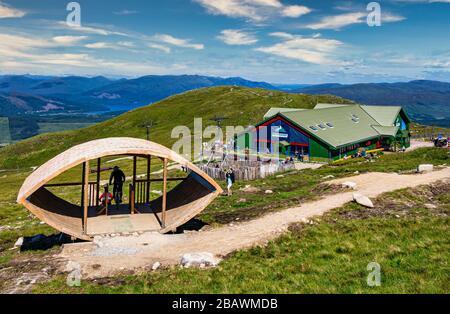 Biker, die von der Talfahrt des Beat Downhill auf der obersten Station der Nevis Range auf dem Berg Aonach MOR in der Nähe von Fort William Scotland mit dem Gebäude der Nevis Range abfahren Stockfoto