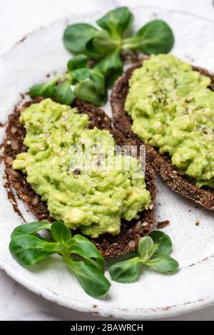 Roggenbrot mit gemahlen Avocado- und Hanfsamen. Gesunder veganer Avocado-Toast auf weißem Teller Stockfoto