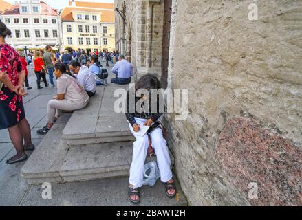 Eine Frau sitzt auf den Stufen des Rathausgebäudes in Tallinn am Altstädter Ring und schreibt Postkarten an einem überfüllten Tag im mittelalterlichen Estland von Tallinn. Stockfoto