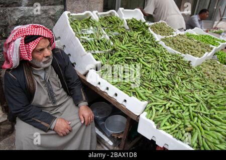 Amman, Jordanien, 3. Mai 2009: Ein Mann in einem traditionellen Thawb und einer Kufiya verkauft grüne Bohnen auf einem Straßenmarkt in Dowtown Amman, Jordanien. Stockfoto