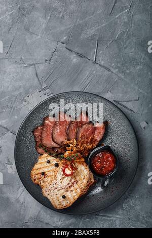 Saftiges Roastbeef mit Ciabatta in Tomatensauce ist schön geschnitten und auf Tellern ausgelegt. Draufsicht, schöne Tischeinstellung, schöne Portion Stockfoto