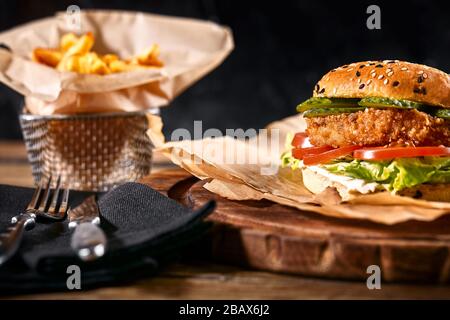 Saftiger Burger auf dem Brett, schwarzer Hintergrund. Dunkler Hintergrund, Fast Food. Traditionelle amerikanische Küche. Speicherplatz kopieren. Stockfoto