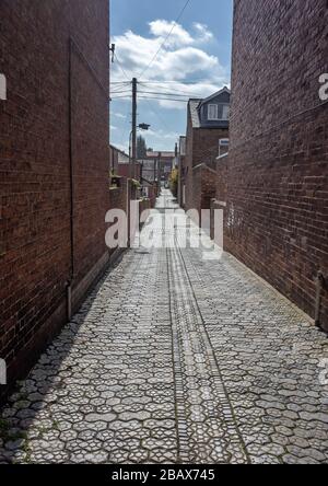 Eine gepflasterte Gasse zwischen rot gemauerten Gebäuden, die in die Ferne führt. Stockfoto