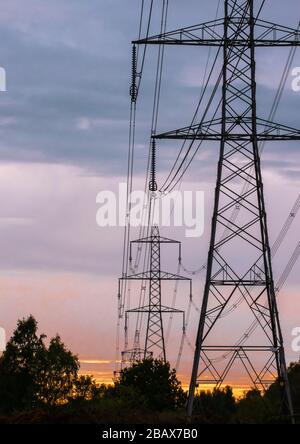 Eine Silhouettenlinie mit Strommasten mit orangefarbenem Sonnenuntergang. Stockfoto