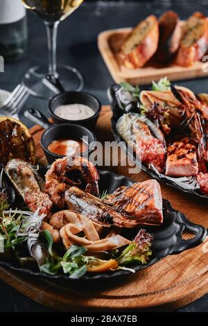 Verschiedene Meeresfrüchte auf Teller. Schöne Komposition auf einem Tisch mit Meeresfrüchten, Tintenfisch, Garnelen, Lachssteak und Tintenfisch. Lebensmittelfoto, niedrige Tonart, traditionell Stockfoto