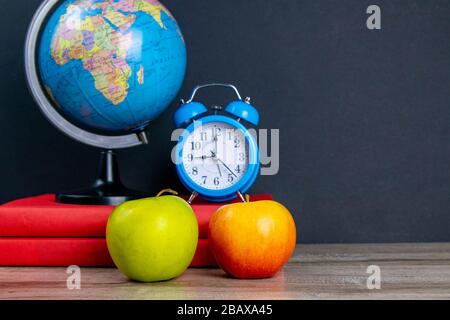 Der Globus und die blaue Uhr stehen auf einem Stapel Bücher, neben einem apfel Stockfoto