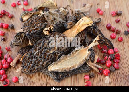 Haufen getrockneter Morchella conica- oder Morel-Pilze mit roten Pfefferkörnern auf Bambushackbrett Stockfoto
