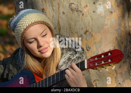 Portrait von Young. Schönes Mädchen mit niedlicher Wollmütze und Gitarre unter großem Planetenband, natürlicher Look Stockfoto