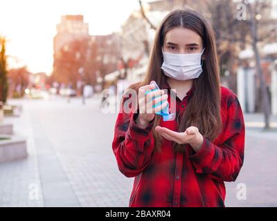 Ernsthafte Frau, die Desinfektionsmittel aus einer tragbaren Flasche zur Desinfektion der Hände anwendet, Mädchen in einer Gesichtsschutzmaske. Desinfektion und erneute Desinfektion der Hände Stockfoto