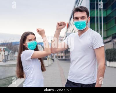 Ellenbogenschlag. Zwei Frauen, Mann mit medizinischer Maske, Freunde grüßen sich mit Ellbogen, anstatt die Hände zu schütteln, die auf die Kamera schauen, die das n zeigt Stockfoto