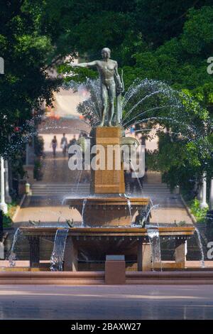 Der Archibald Fountain befindet sich im Hyde Park in Sydney, Australien. Benannt ist es nach J.F. Archibald, der Gelder vermachte, um sie bauen zu lassen. Archibald legte fest, dass es von einem französischen Künstler aufgrund seiner großen Liebe zur französischen Kultur entworfen werden muss und um der Vereinigung Australiens und Frankreichs in WW1 zu gedenken. Er wünschte, Sydney strebe nach Pariser Civic Design und Ornamentik. Als Künstler ausgewählt wurde François-Léon Sicard, der es 1926 in Paris fertigstellte, aber nie sah, wie die Skulptur in Sydney aufgestellt wurde, wo sie im März 1932 vom Oberbürgermeister von Sydney, Samuel Walder, enthüllt wurde. Stockfoto