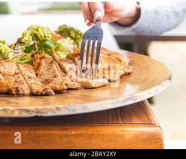 Hühnersalat in einem mexikanischen Restaurant mit einer jungen Dame mit netten Nägeln, die ein Stück Huhn auf einem dunklen Holztisch und hell ausgeblasenen Windo machen Stockfoto