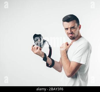 Unglücklich traurig und verärgert halten junge Fotografen professionelle Geräte in der Hand und schauen auf die Kamera. Emotionaler Kerl hält Fotoausrüstung. Kann nicht nehmen Stockfoto