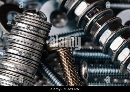 Ein Makroschuss der Gewinde einer kleinen Edelstahlschraube auf einem Stapel von Unterlegscheiben, Muttern und Schrauben. Starker Kontrast im gesamten Bild. Stockfoto