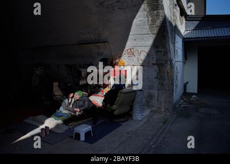 München, Deutschland. März 2020. Gogo sitzt mit seiner Freundin Elli an seinem Schlafplatz unter einer Eisenbahnbrücke, die sie mit gefundenen Gegenständen bequem gemacht haben. Obdachlose sind besonders von der Corona-Pandemie betroffen. Das Hilfesystem zerfällt zunehmend, gleichzeitig müssen die oft immungeschwächten Menschen vor allem eine Infektion fürchten. Credit: Bernd Thissen / dpa / Alamy Live News Stockfoto