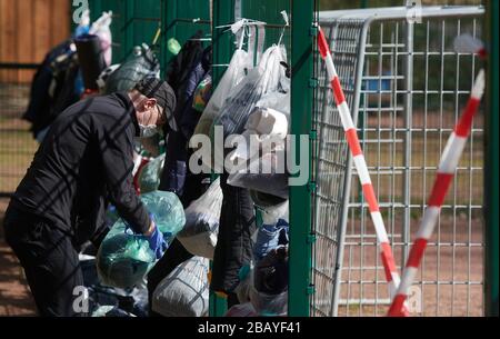 München, Deutschland. März 2020. Björn Boueke ordnet die Sachspenden an, die Bürger an einem sogenannten Geschenkzaun an den Zaun eines Fußballfeldes für Obdachlose gehangen haben. Obdachlose sind besonders von der Corona-Pandemie betroffen. Das Hilfesystem zerfällt zunehmend, gleichzeitig müssen die oft immungeschwächten Menschen vor allem eine Infektion fürchten. Credit: Bernd Thissen / dpa / Alamy Live News Stockfoto