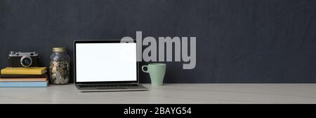 Zugeschnittene Aufnahme eines eleganten Arbeitsbereichs mit aufgemanagtem Laptop, Kamera, Büchern und Platz für Kopien auf dem Marmorschreibtisch mit grauer Loftwand Stockfoto