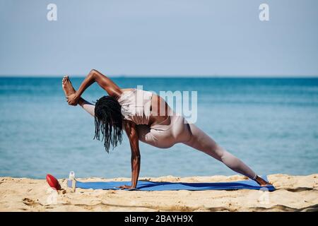 Passen Sie die junge Frau, die Visvamitrasana macht, sie streckt das Bein zur Seite und hält den Fuß mit der Hand Stockfoto