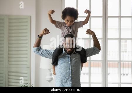 Afrikanische Ethnie kleiner Sohn, der auf den Schultern der Väter sitzt und Bizeps zeigt Stockfoto
