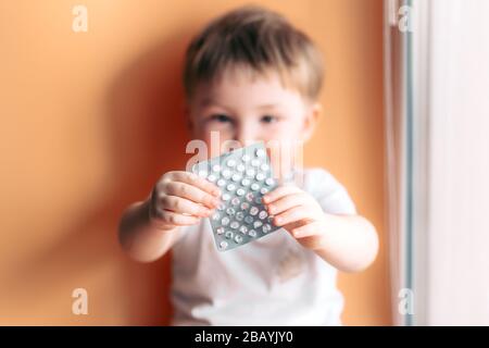 Ein kleines Kind Kleinkind Baby Junge hält einen Teller mit Pillen in seinen Händen ausgewählt Fokus auf Pillen Kind unfokussiert Stockfoto