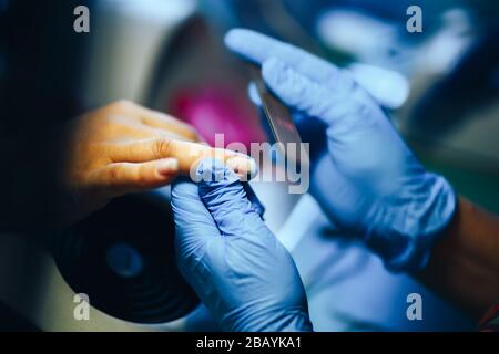 Manikuristenmeister machen Maniküre in blauen Handschuhen mit Nagelfeile. Frau erhält Nagelmaniküre Stockfoto