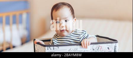 Hübsches Baby Kleinkind Junge oder Mädchen, das in einer Kiste in der Wohnung sitzt Stockfoto