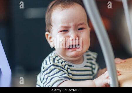 Weinendes kleines Cutie drk-haariges Mädchen, steht laut weinend, in der Nähe des Stuhls zu Hause Stockfoto